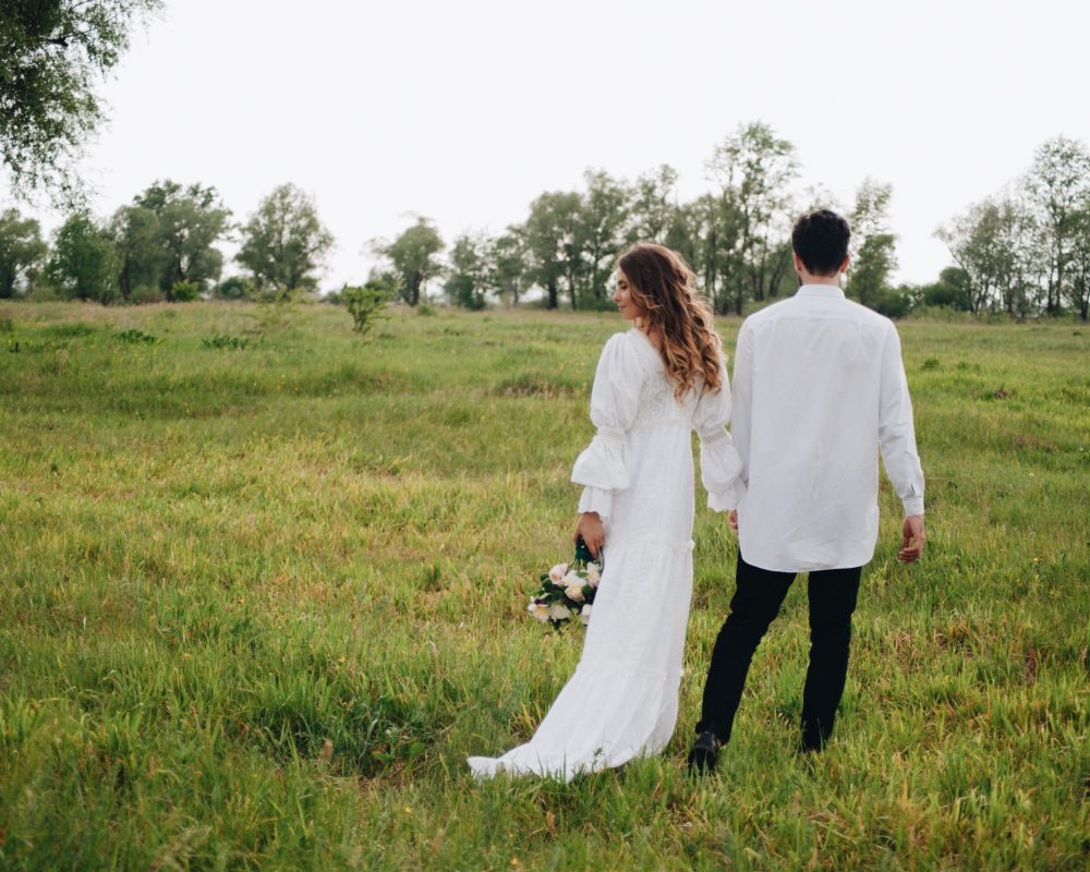 Hochzeitspaar steht auf einer Wiese im Hintergrund stehen Bäume.